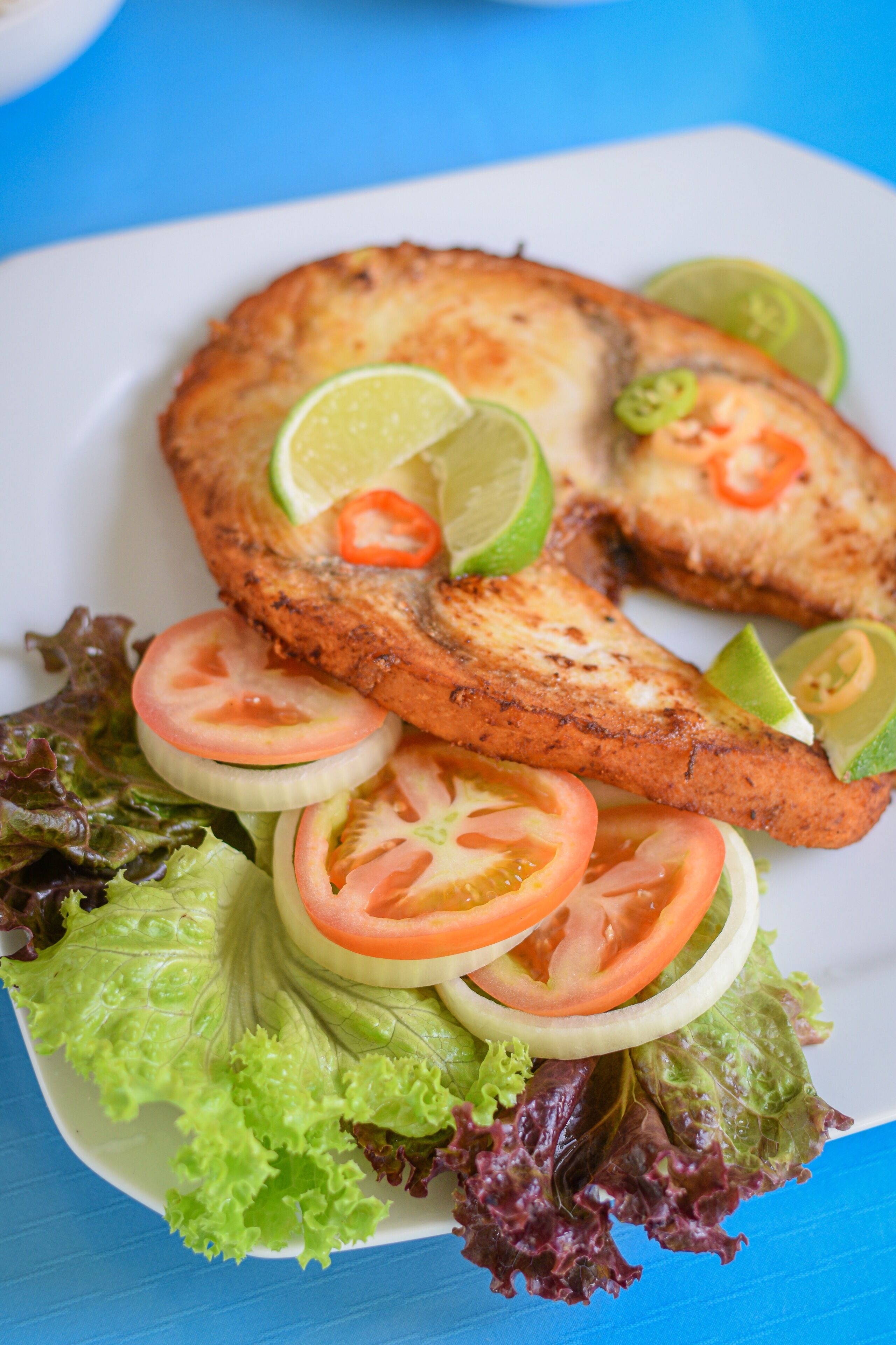 Un plato con pescado a la parrilla, lechuga, tomates y gajos de lima.