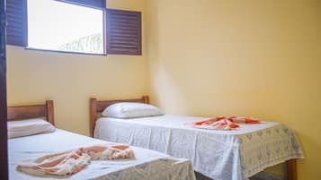 Two single beds with wooden headboards, a window with shutters, and a table with a tablecloth.