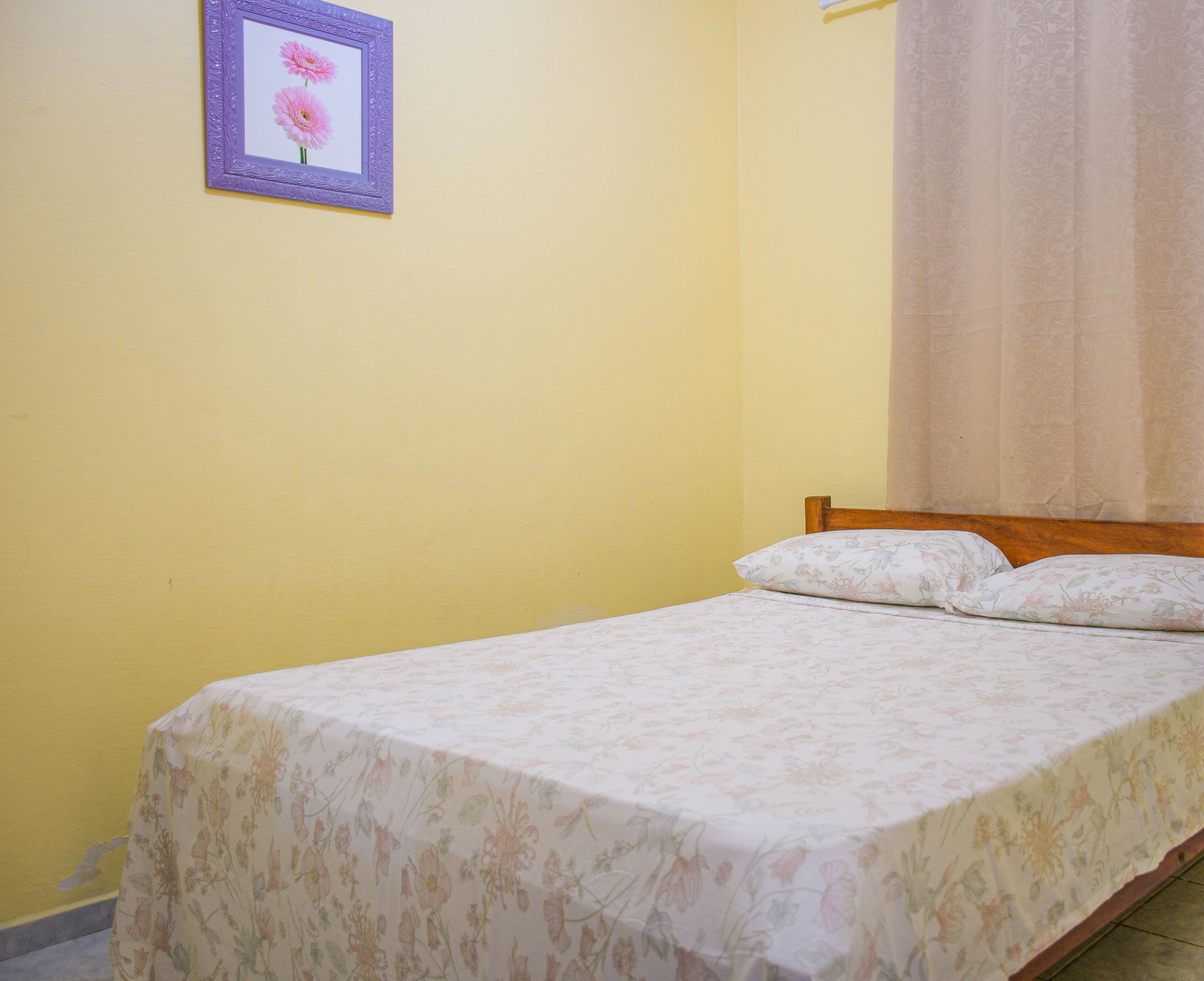 A single bed with floral bedding, a wooden headboard, and a framed picture on the wall.