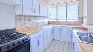 A kitchen with white cabinets, a gas stove, a window, and a sink. - Rentamos Aparta Estudio for Short or lon (Santo Domingo)