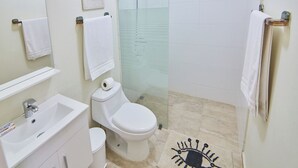 A bathroom with a sink, toilet, and shower. There are towels hanging on the wall and a glass shower door. - Rentamos Aparta Estudio for Short or lon (Santo Domingo)