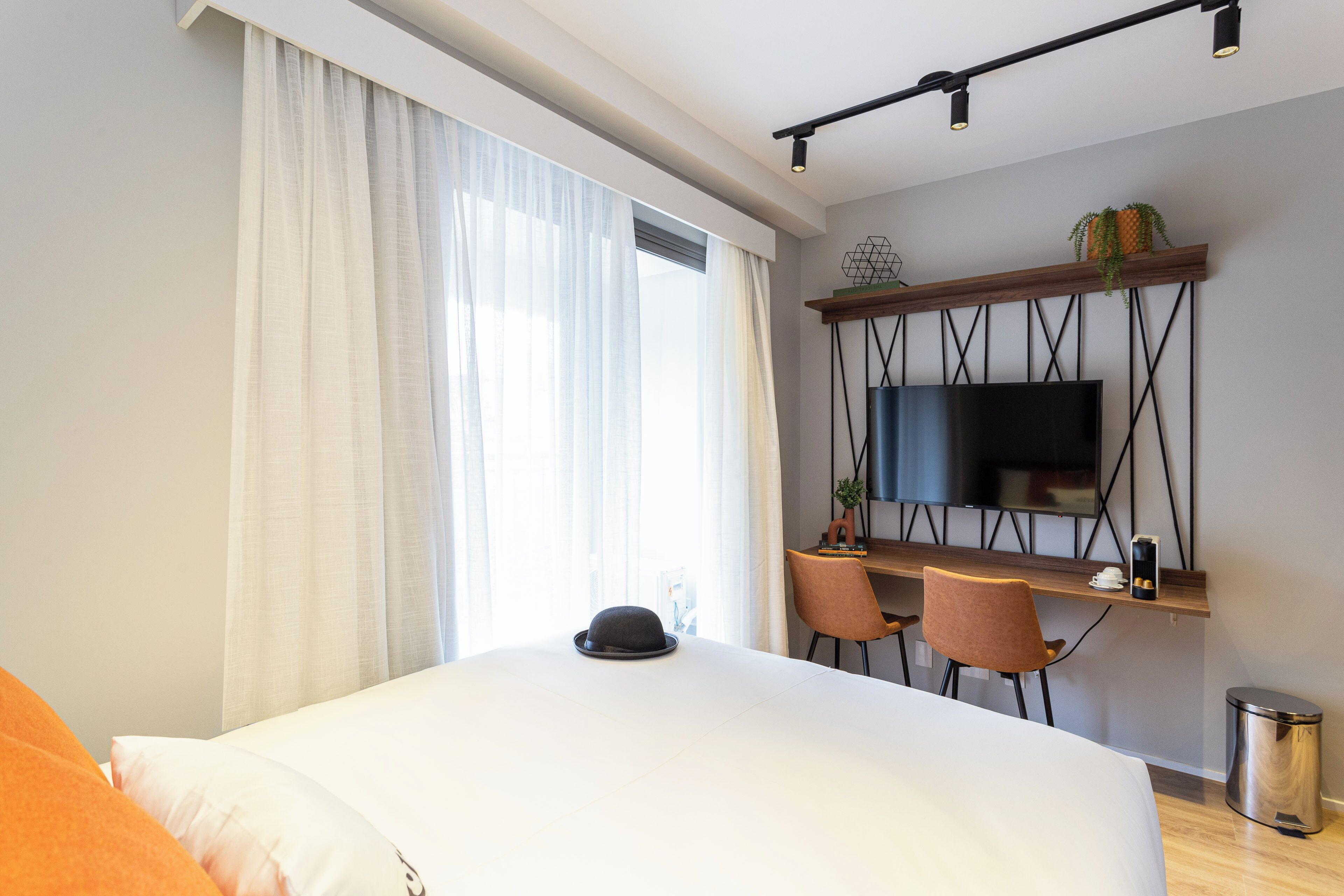 Une chambre d’hôtel moderne dotée d’un grand lit, d’un bureau avec deux chaises, d’un téléviseur fixé au mur et d’une fenêtre avec des rideaux.