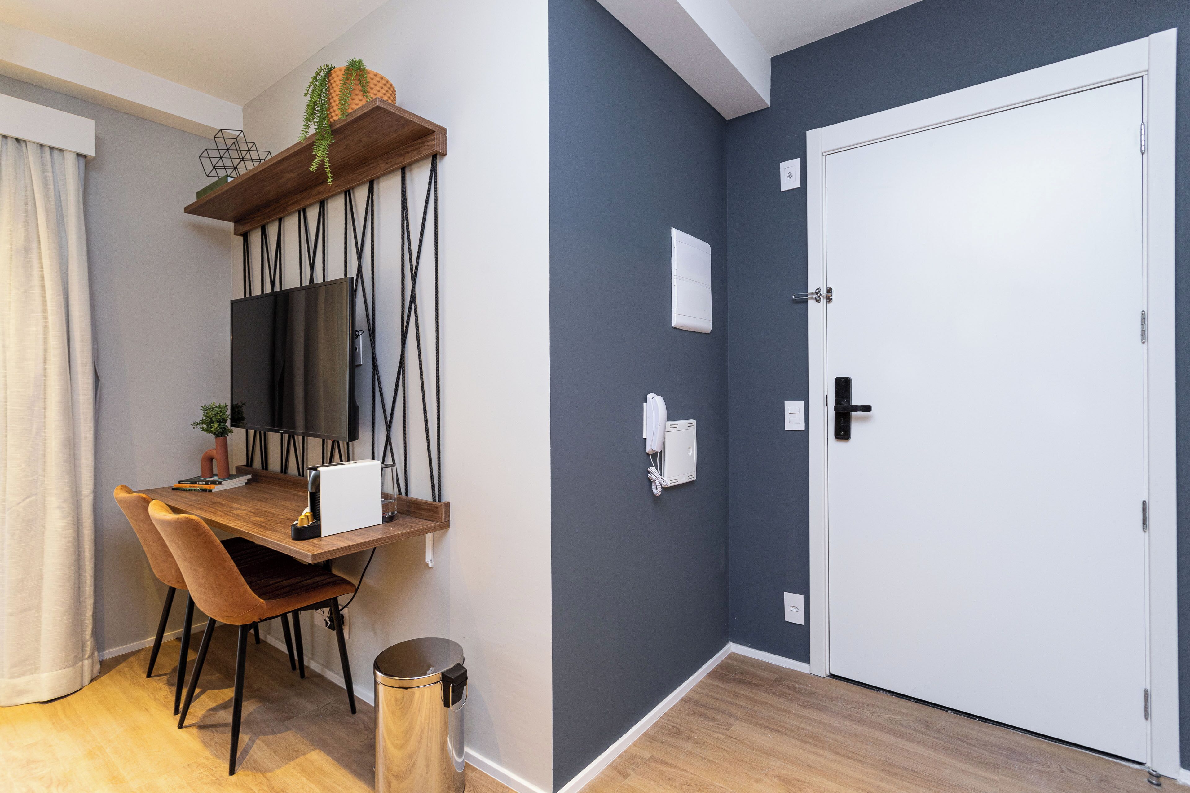 A modern room with a wooden desk, two chairs, a TV, a white door, and a grey wall.