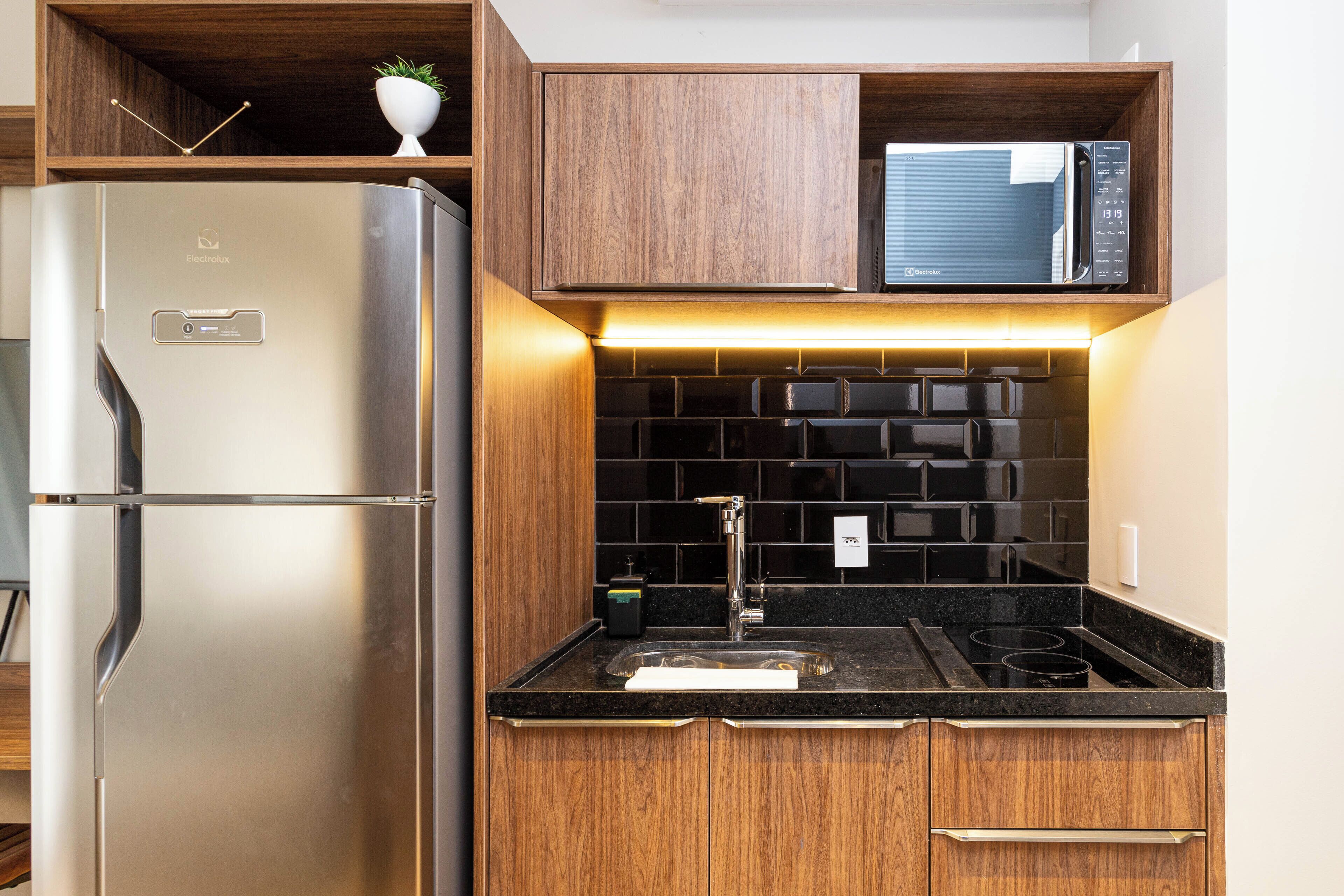 Uma cozinha moderna com geladeira de aço inoxidável, micro-ondas e painel de azulejos pretos.