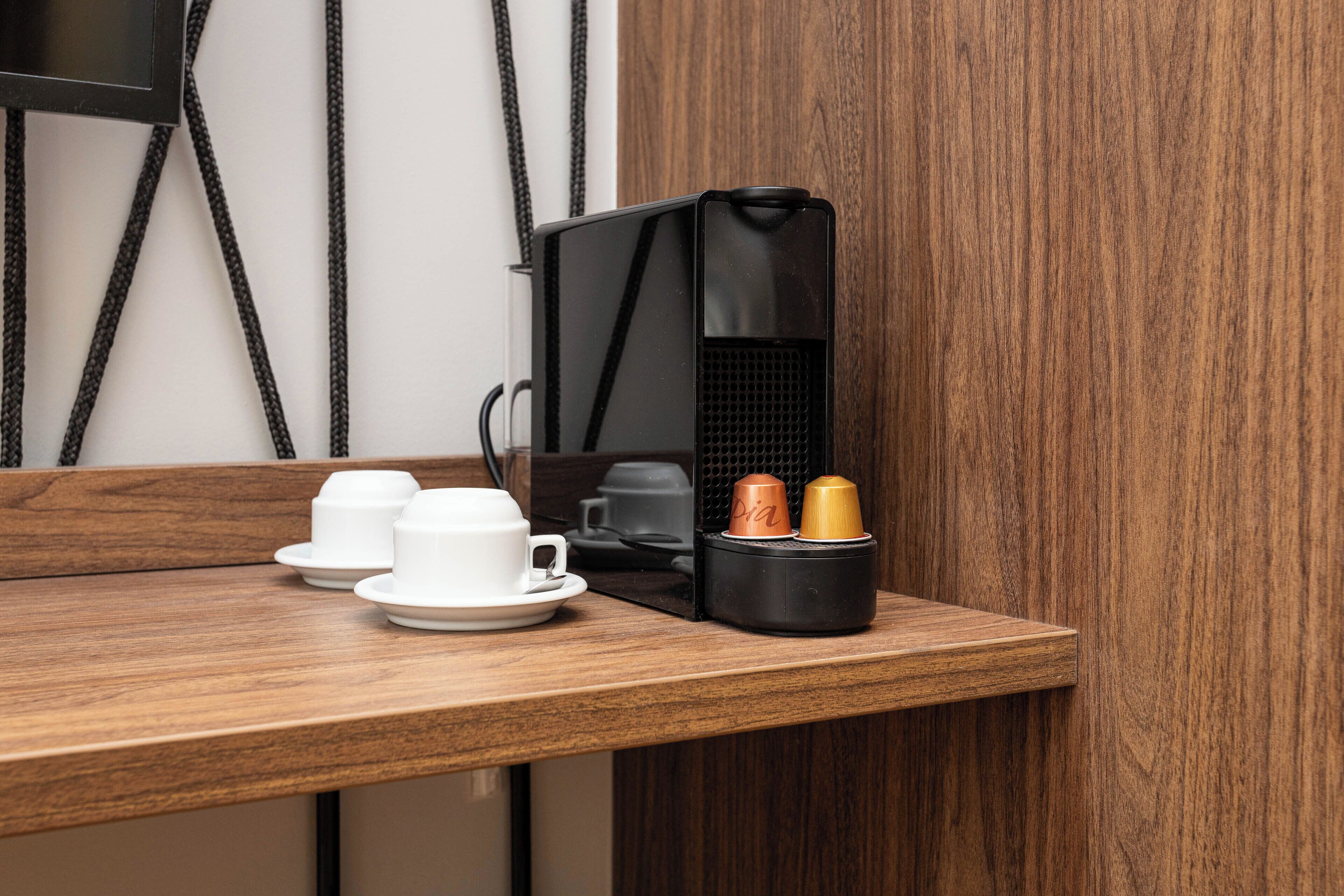 A wooden counter with a black coffee machine, two white cups, and two coffee cups.