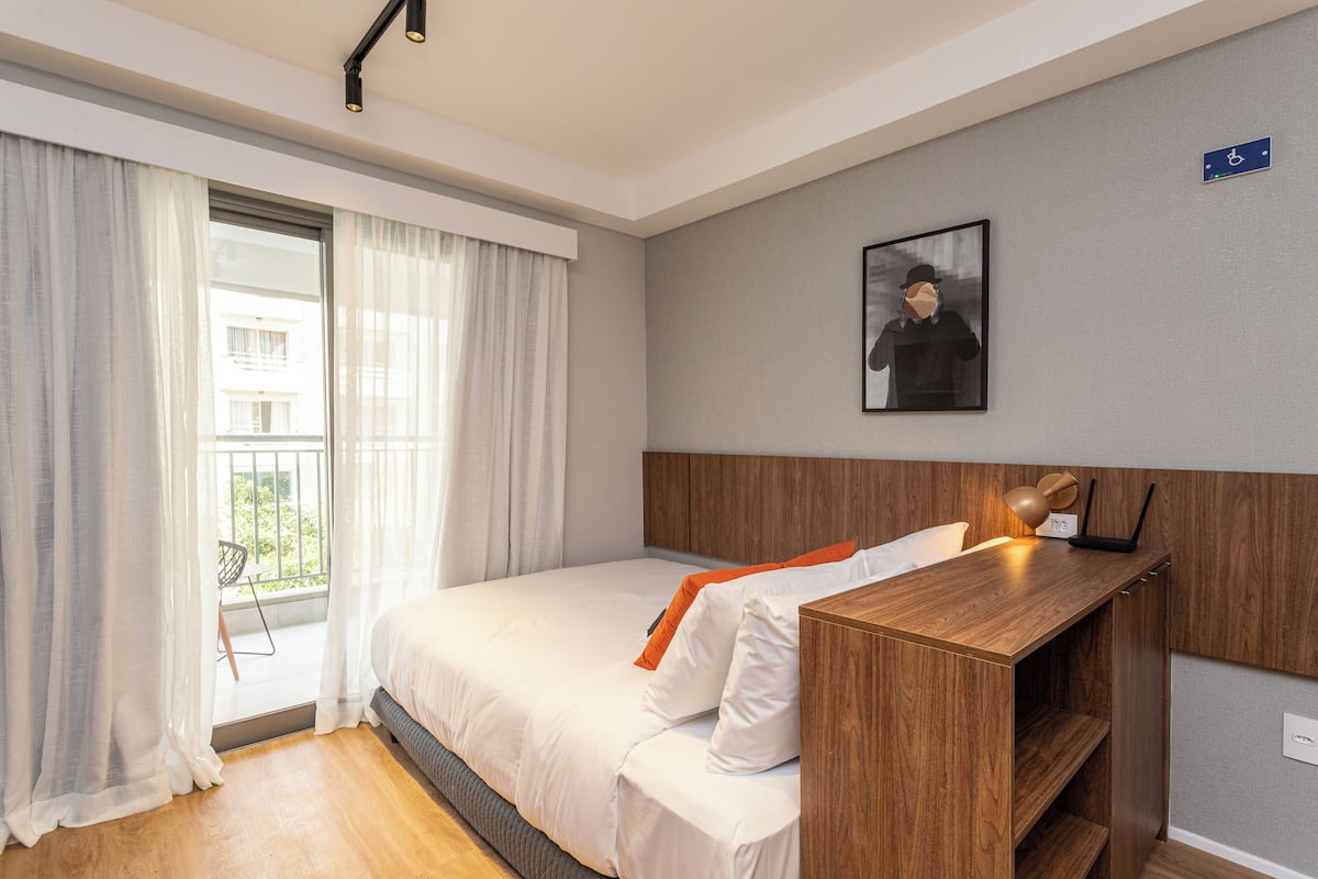 A modern hotel room with a large bed, a wooden desk, and a view of the outdoors.