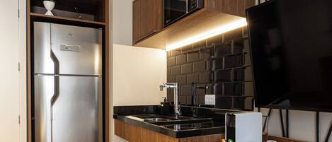 A modern kitchen with a built-in refrigerator, wooden cabinets, a black countertop, and a flat-screen TV.