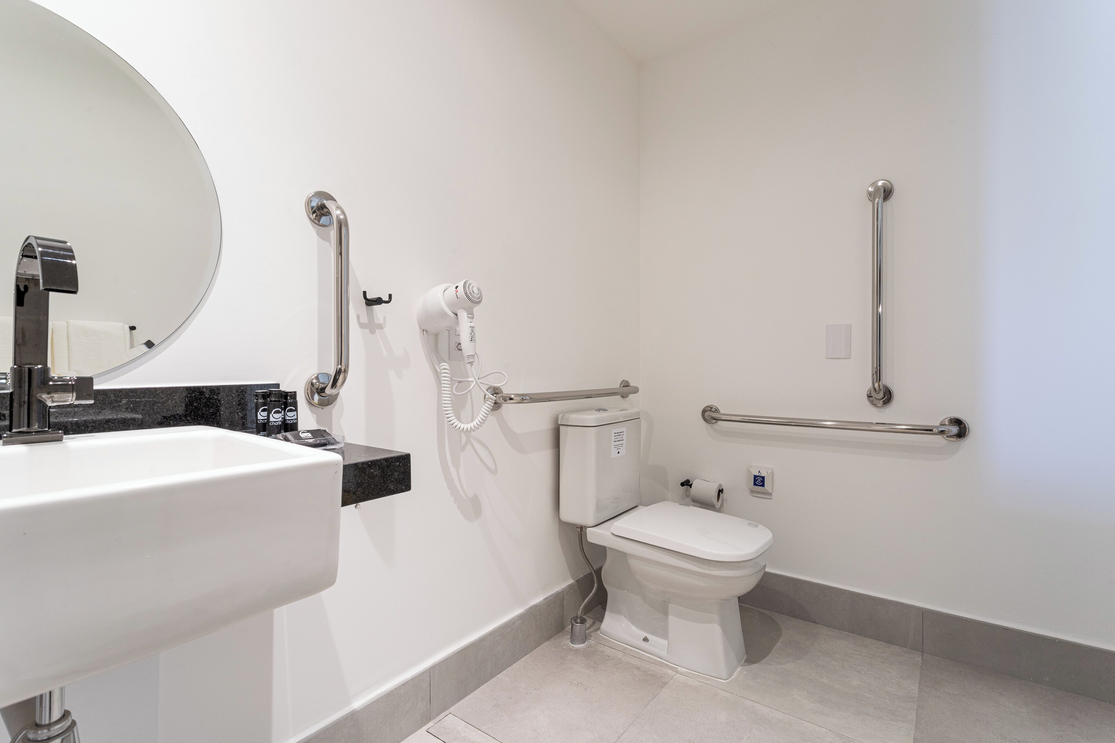 Een moderne badkamer met een wit wastafel, toilet en bidet, voorzien van handgrepen en een spiegel.
