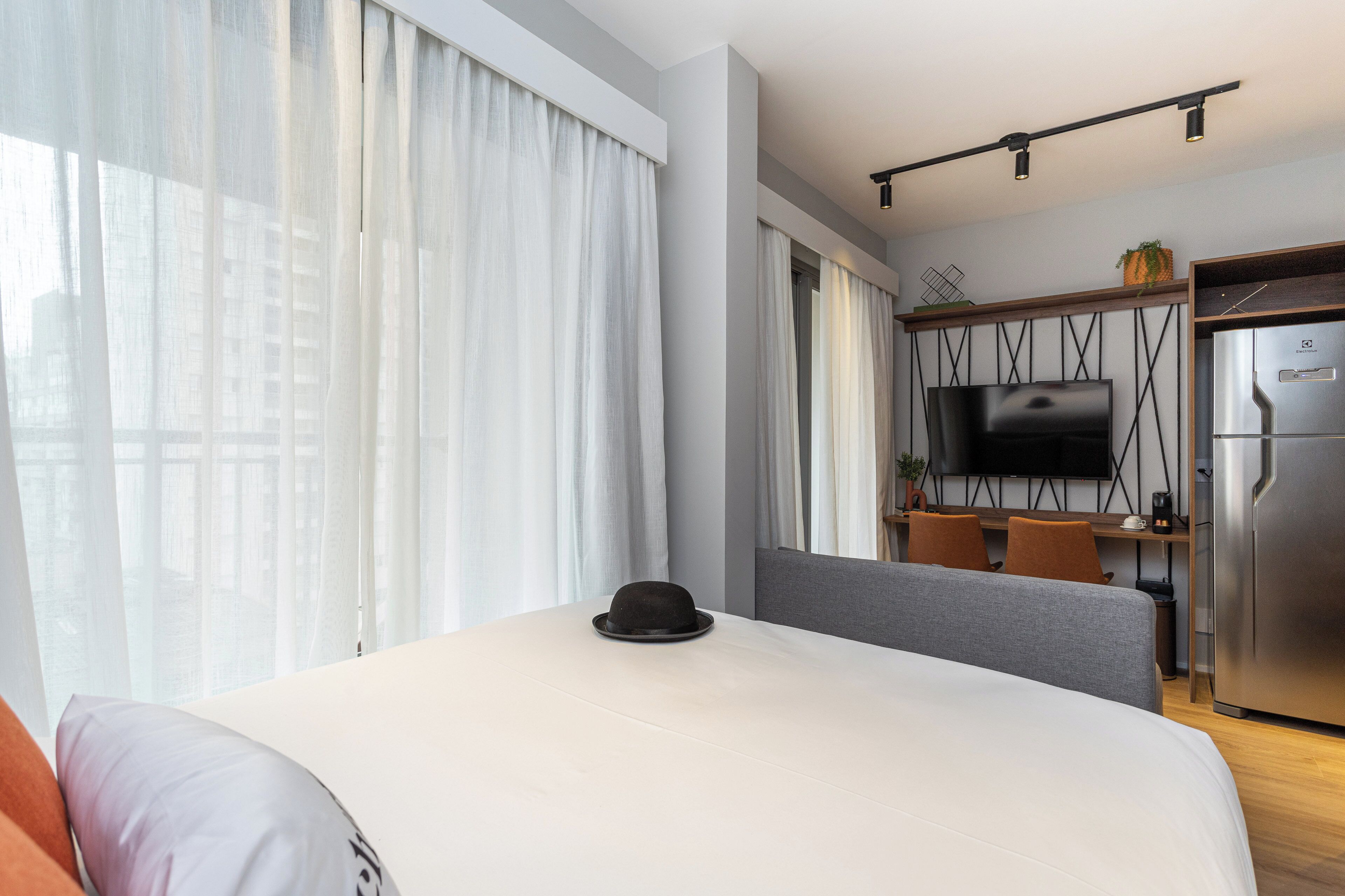 Quarto de hotel com cama, uma mesa de jantar com cadeiras, televisão e frigorífico.