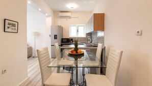 A compact kitchen with a refrigerator, microwave, and a small dining area with a glass table and white chairs.