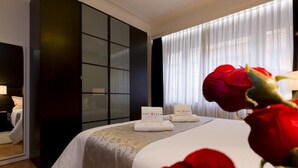 Una habitación de hotel con una cama, un espejo grande, un armario y una ventana con cortinas translúcidas.