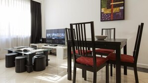 Una sala moderna con una mesa de comedor de vidrio, sillas negras con cojines rojos, un televisor de pantalla plana y una cafetera.