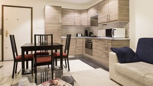 Una cocina compacta con electrodomésticos modernos, una zona de comedor con una mesa de vidrio y un sofá.