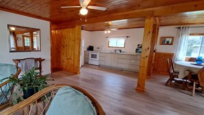 Una habitación acogedora con techo de madera, un comedor con mesa y sillas, una cocina con estufa y lavaplatos, y un espejo grande en la pared.