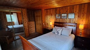Un dormitorio con paneles de madera, una cama, dos lámparas de noche, un tocador y una silla.