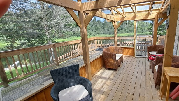 Una terraza de madera con mobiliario de mimbre y una mesa, con vistas a una zona boscosa.
