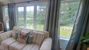 Un salón con un sofá a rayas, un sillón marrón y vistas a un jardín a través de grandes ventanales.