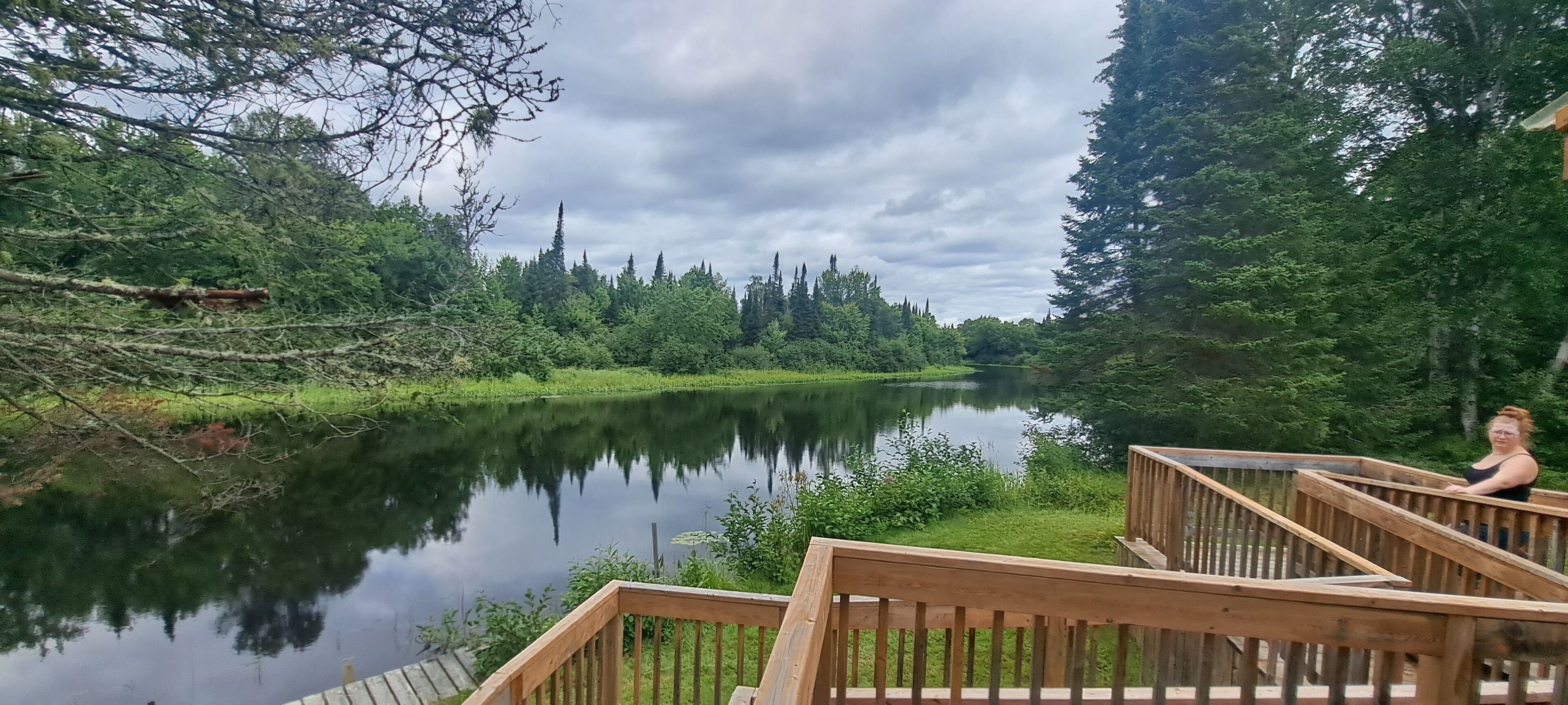 A wooden deck overlooking a calm river with dense forest on both sides.