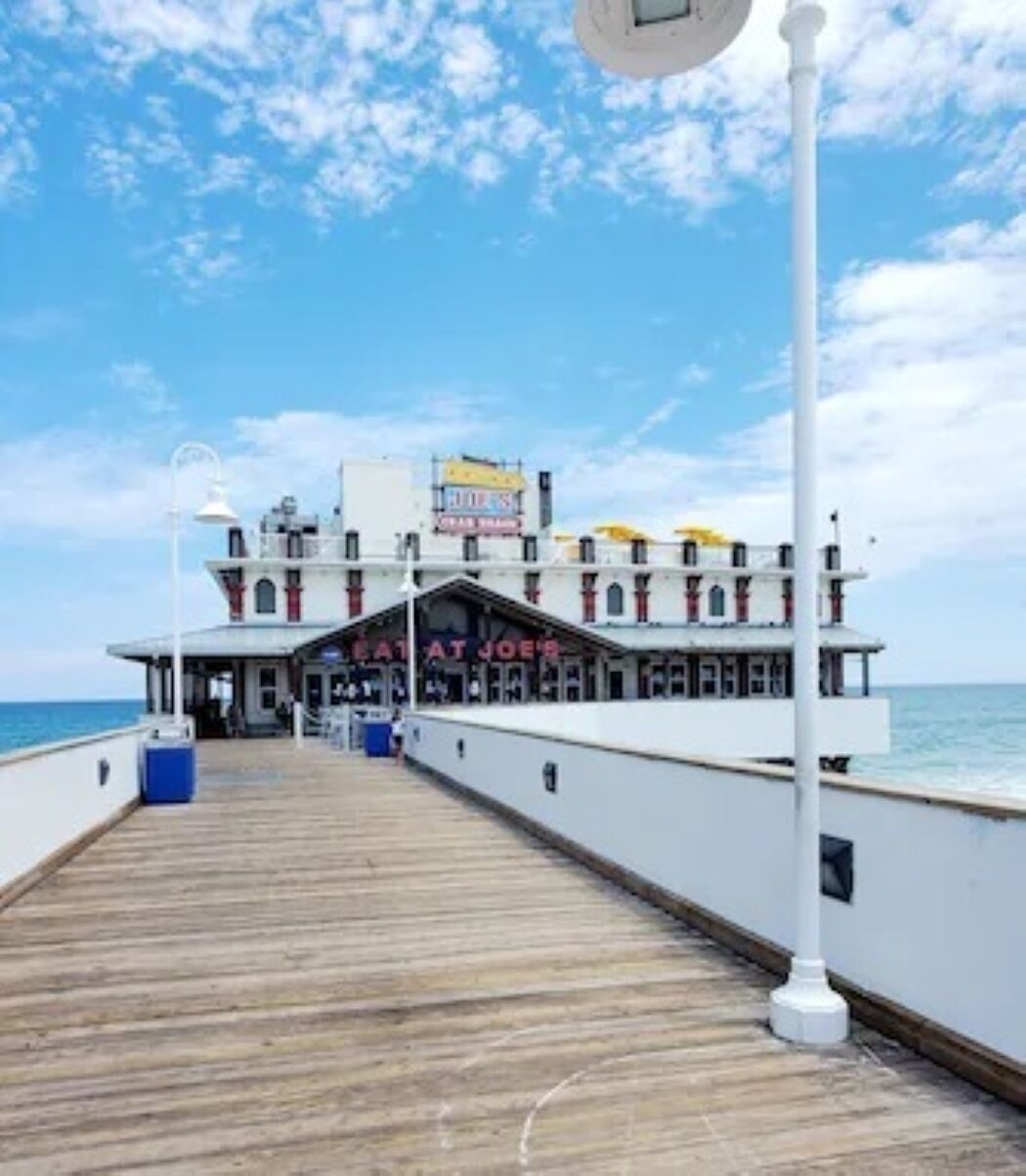 A pier leading to a multi-story building with a sign reading 'Eat at Joe's.'