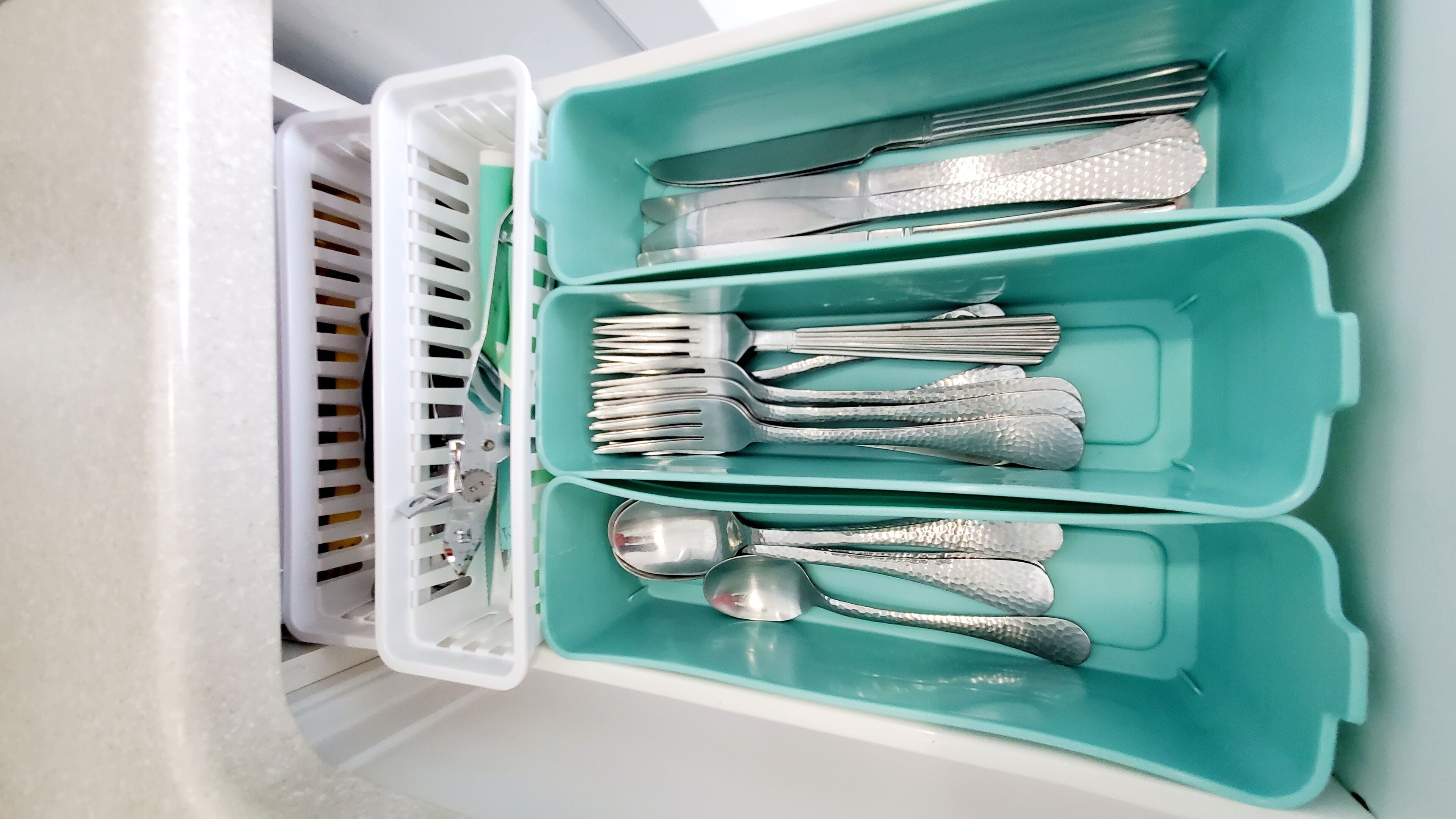 A drawer with teal compartments containing silverware, including forks, knives, and spoons.