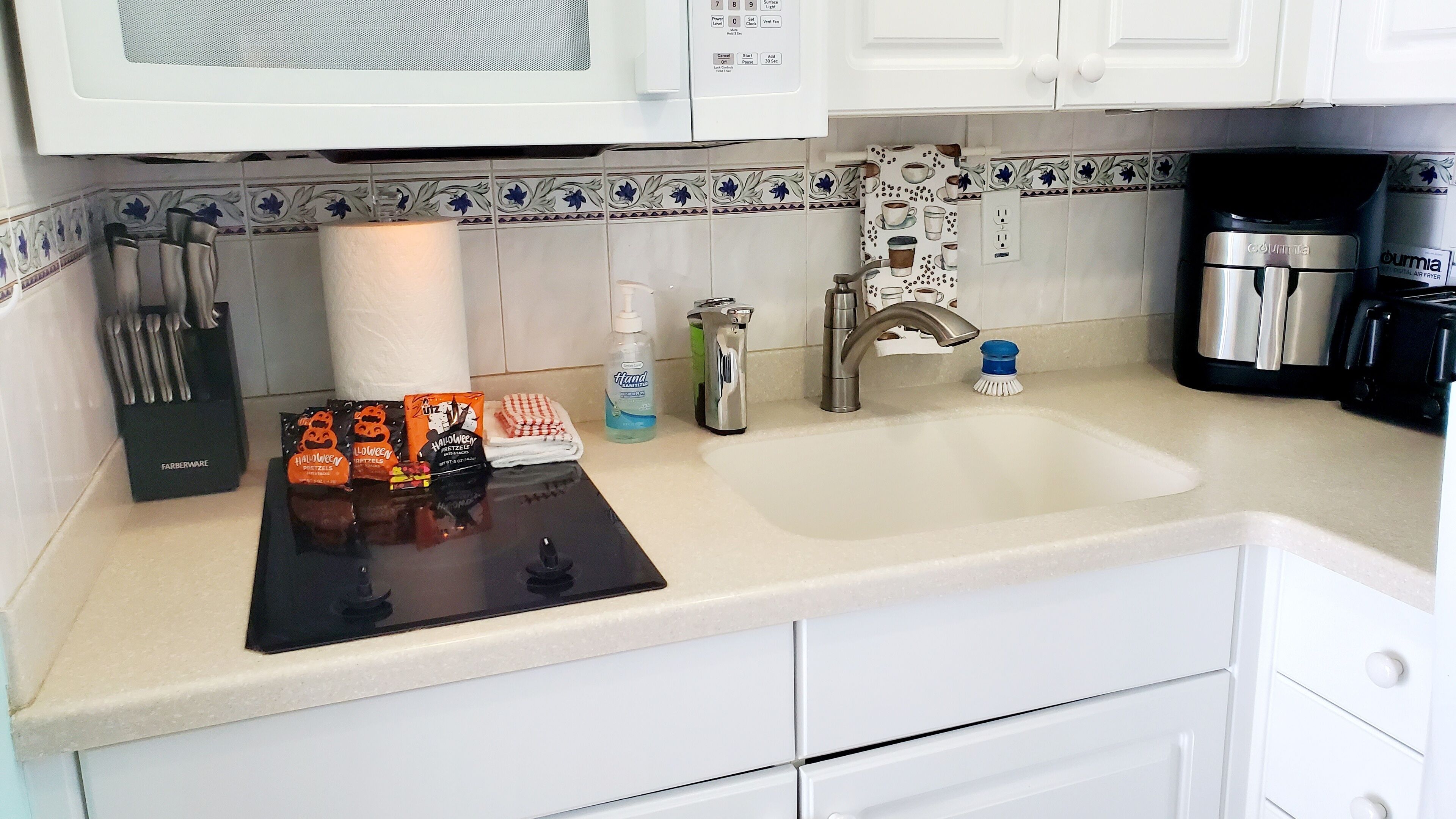 Una cocina con armarios blancos, microondas, cafetera y fregadero.