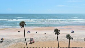 Een strand met palmbomen, een redderpost en strandparasols.