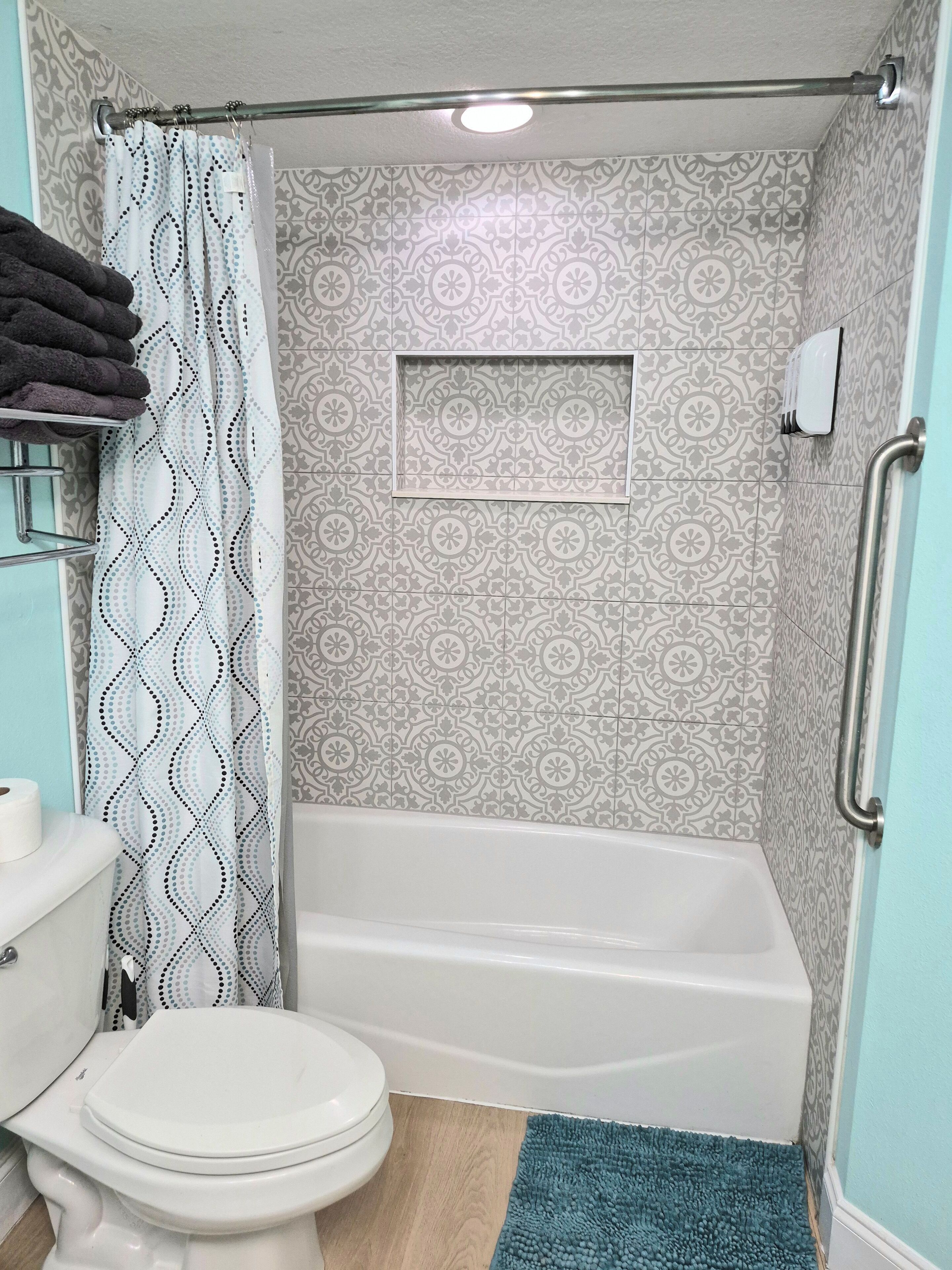 A bathroom with a toilet, a bathtub, a shower curtain, and a handrail.