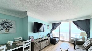 Een woonkamer met een televisie, een eettafel, stoelen, een bank en een balkon met uitzicht.