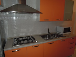 A kitchen with a gas stove, stainless steel sink, and a microwave.