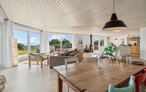 A spacious living area with a wooden dining table, a sofa, and a view of the outdoors through large windows. - Awesome home in Kalundborg with WiFi (Kalundborg)