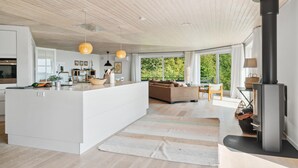 Una cocina moderna con una isla central, un rincón de comedor con sofá, y un amplio ventanal con vistas al verdor.