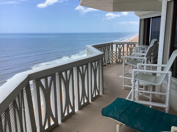A balcony with a view of the ocean, white chairs, and a green cushion. - Oceanfront PENTHOUSE! Large Pool, Private Beach Access! Family Friendly! (Ormond Beach)