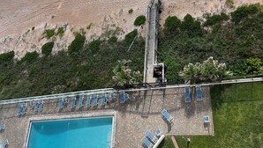 An aerial view of a resort with a swimming pool, beach access, and a staircase leading to a balcony. - Oceanfront PENTHOUSE! Large Pool, Private Beach Access! Family Friendly!  (Ormond Beach)