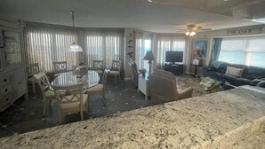 A spacious living area with a dining table, chairs, a sofa, and a TV. - Oceanfront PENTHOUSE! Large Pool, Private Beach Access! Family Friendly!  (Ormond Beach)