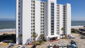 A multi-story hotel with a white facade, located near a beach with a parking lot in front. - Oceanfront PENTHOUSE! Large Pool, Private Beach Access! Family Friendly!  (Ormond Beach)