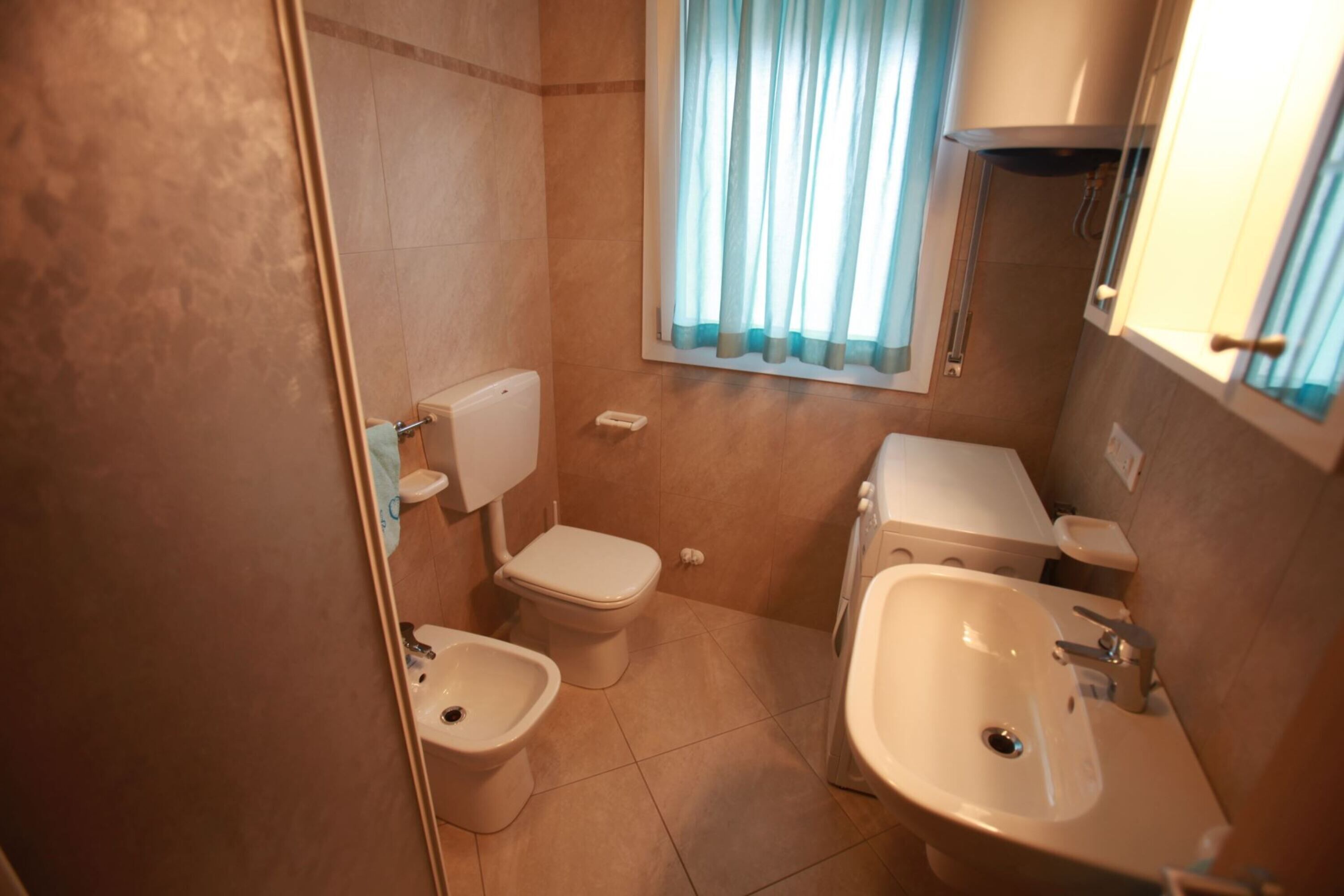 Ein Badezimmer mit Toilette, Bidet, Waschbecken und Fenster mit Vorhängen.