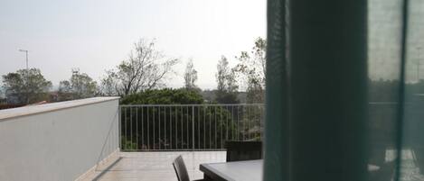 A balcony with a table and chairs, a railing, and a view of trees and buildings.