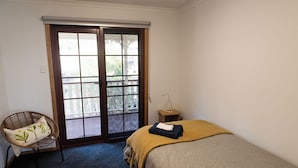 Quarto com cama, cadeira, mesa de cabeceira e porta de correr para uma varanda.