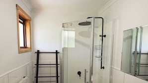 Um banheiro moderno com box de vidro, toucador de madeira com pia branca e porta-toalhas com toalhas.