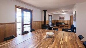 Uma sala de conferência com uma grande mesa de madeira, cadeiras pretas e uma tigela branca. Há um sofá e uma mesa de centro ao fundo.