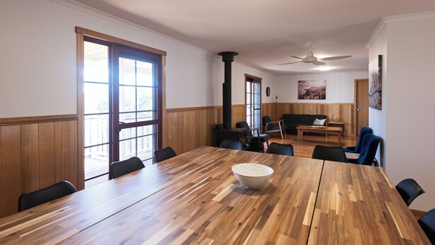A conference room with a large wooden table, black chairs, and a white bowl. There is a sofa and a coffee table in the background.