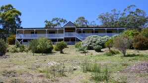 A two-story building with a balcony on the upper floor, surrounded by trees and shrubs.