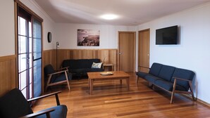 Um quarto com piso de madeira, um sofá, uma mesa de centro e uma TV fixada na parede.