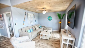 A living room with a wooden ceiling, a beige sofa, a white coffee table, and a TV mounted on the wall. - NEW: Beach House 3-Bed/2-Bath with Ocean View & Golf Cart -- Great Beach (Surfside Beach)