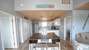 A spacious kitchen with a wooden table and white bar stools, a dining area with a wooden ceiling, and a sign reading "Surfside Beach". - NEW: Beach House 3-Bed/2-Bath with Ocean View & Golf Cart -- Great Beach (Surfside Beach)