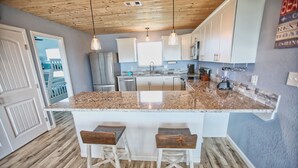 A kitchen with granite countertops, white cabinets, and wooden stools. - NEW: Beach House 3-Bed/2-Bath with Ocean View & Golf Cart -- Great Beach (Surfside Beach)