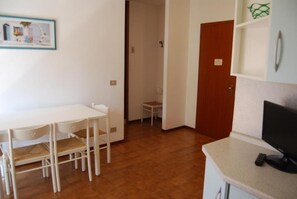 Een kamer met een witte tafel en stoelen, een televisie en een deur naar een andere kamer.
