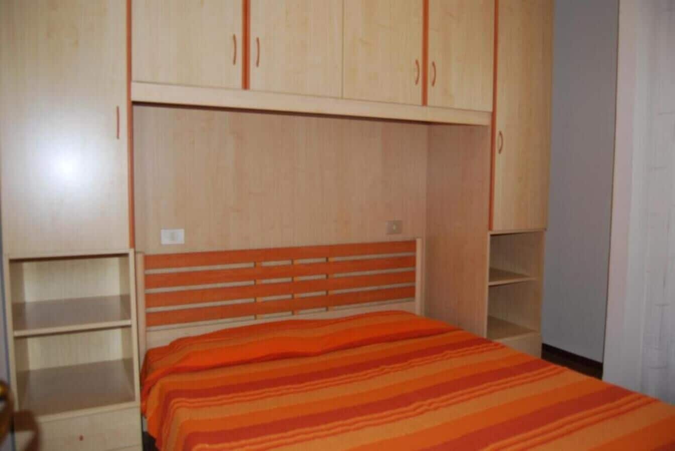 Een slaapkamer met een bed, een houten garderobe en inbouwplanken.
