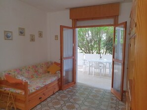 A room with a wooden sofa, a dining table, and chairs outside a glass door.