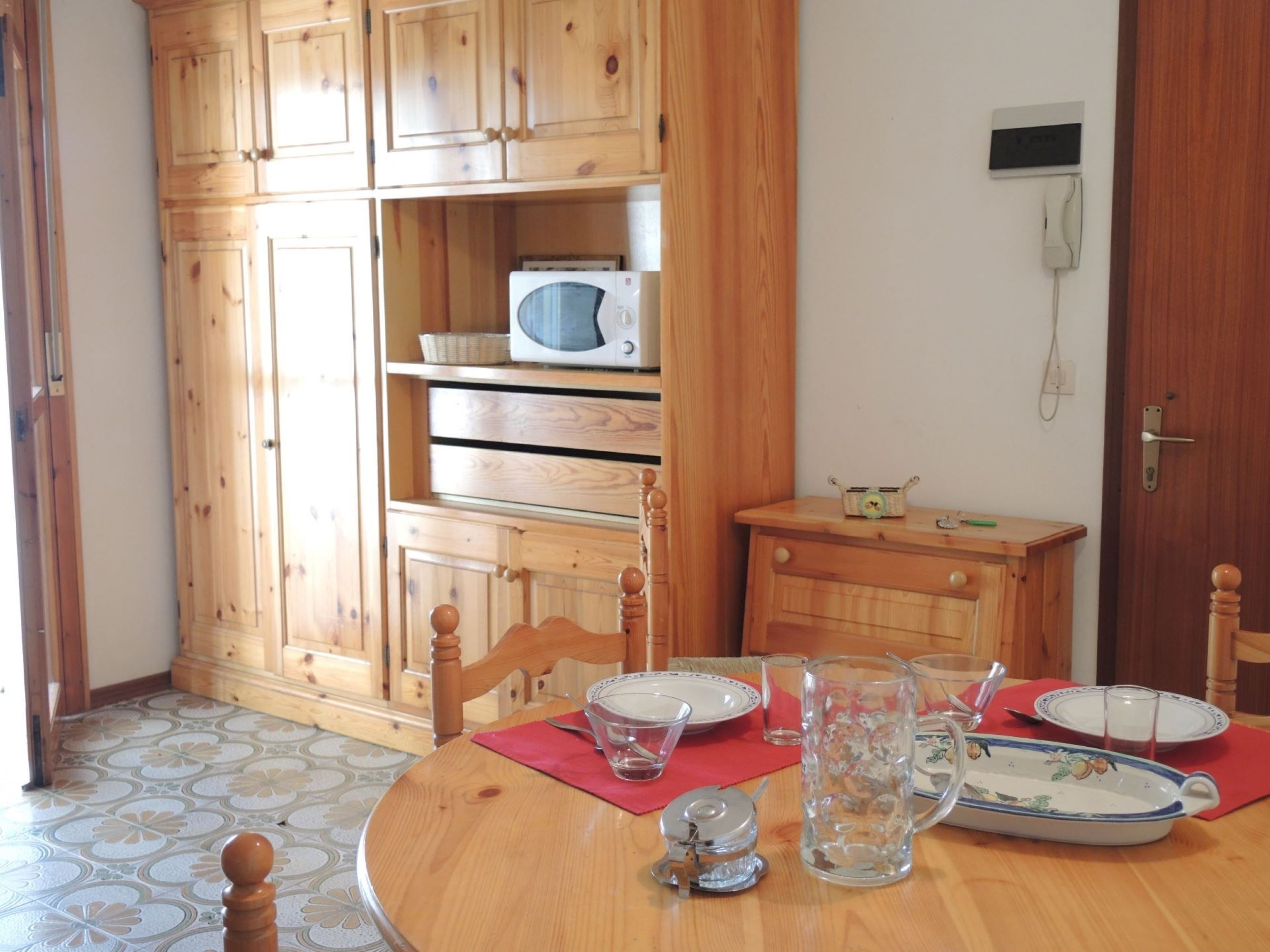 A dining area with a wooden table set for four, surrounded by wooden cabinets and a microwave.